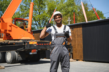 Construction worker supervising lifting of modular house onto truck