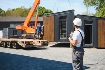 Construction worker controls lifting of modular house onto truck with remote control