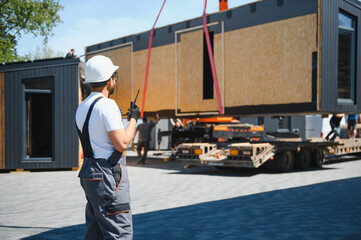 Construction worker supervising loading of modular house onto truck
