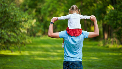 Father carrying daughter on shoulders in sunny park