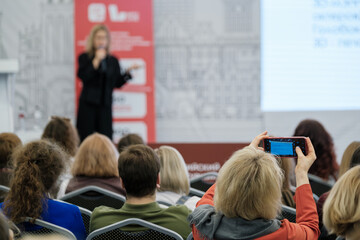 Conference attendees listening to a speaker while one records the session using smartphone.