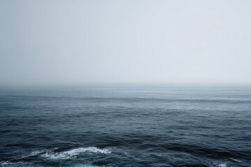 A misty, grey ocean stretches to a hazy horizon, subtle waves lapping at the unseen shore. The somber palette evokes a sense of quiet solitude