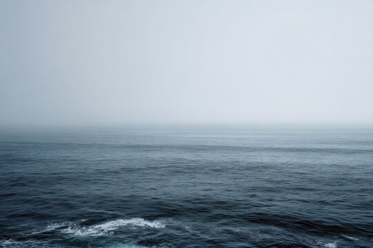 A misty, grey ocean stretches to a hazy horizon, subtle waves lapping at the unseen shore. The somber palette evokes a sense of quiet solitude