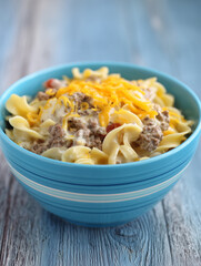 Creamy hamburger noodle casserole with grated cheese topping in blue bowl