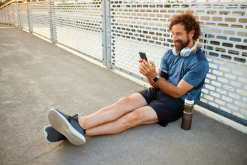 A man sits on a smooth surface, taking a moment to relax after exercise. He is smiling and looking...