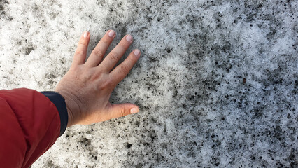 Hand touches the icy surface of Solheimajokull Glacier in Iceland, capturing a personal moment with nature's raw and melting beauty.