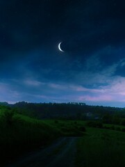 Half moon in the starry sky above the clouds. Night landscape with moon over green hills. Dreamy view.