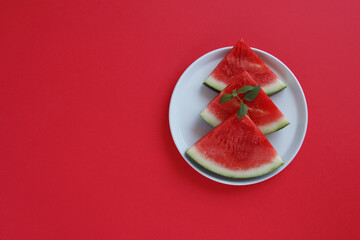 Stacked watermelon slices with mint on white plate and red background