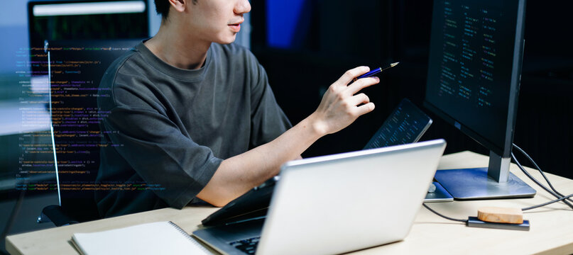 Asian developer writing code at night in modern office setup. Concept of software engineering, programming, digital workspace
