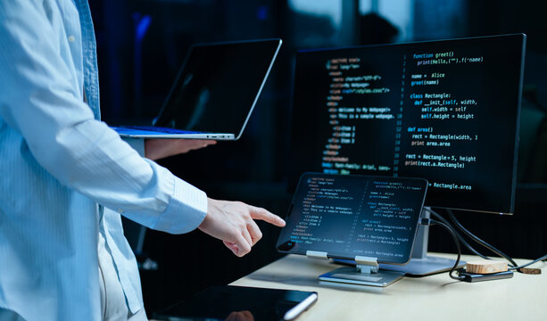 Young male programmer working with tablet and screen displaying code. Modern tech office setup, great for software