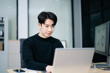 Asian man using laptop and tablet while sitting at her working place. Concentrated at work.