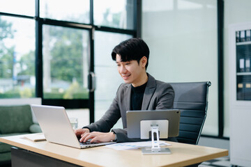 Confident young Asian businessman analyzing financial charts on laptop. Perfect for stock themes in business, finance