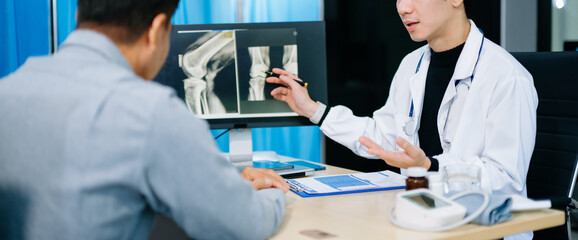 Asian doctor discusses knee X-ray results with senior patient in modern clinic. Concept of...