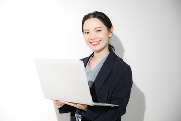 Business image of a young pretty woman standing in a suit with a computer, looking at the camera, upper half of her body.