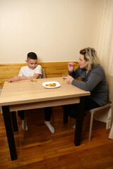 Mother and son drinking tea with pastries at the table in the kitchen.