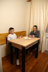 Mother and son drinking tea with pastries at the table in the kitchen.