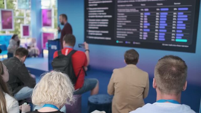 Group of people attending a presentation with screens showcasing multimedia visuals in bright venue.