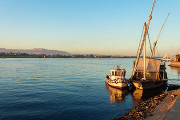 Fototapeta premium Traditional felucca boats moored on the Nile River at golden hour in Luxor, Egypt with mountain view