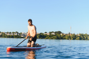 Man kneeling on paddle board rowing in a lake on a sunny day