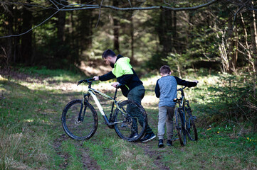 Fototapeta premium Father and son pushing muddy bikes on a forest trail. A sunny day of outdoor adventure.
