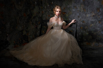 Young pretty blonde with exquisite makeup and hairstyle in a beautiful wedding dress posing sitting...