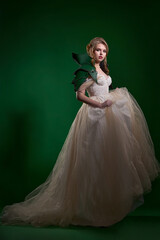Young pretty blonde with exquisite makeup and hairstyle in beautiful wedding dress and green...