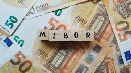 Obraz premium MIBOR acronym made of wooden letter cubes on pile of Euro banknotes. Milan Interbank Offered Rate (Benchmark interest rate for interbank loans)
