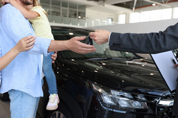 Salesman giving car key to family in salon, closeup