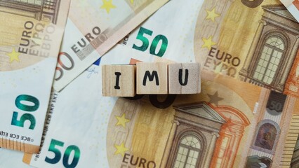 IMU acronym made of wooden letter cubes on pile of Euro banknotes. Imposta Municipale Unica (Unified Municipal Tax, property tax)