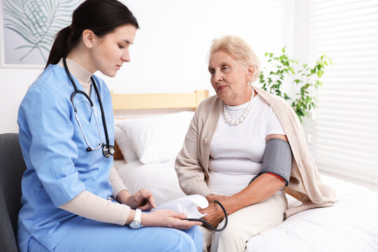 Nurse measuring patient's blood pressure indoors. Home health care service