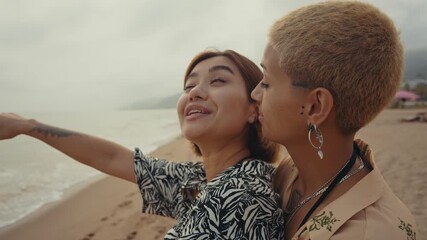 Passionate lesbian couple sharing tender moment while embracing and kissing on sandy beach during romantic sunset, expressing deep love and connection - Powered by Adobe