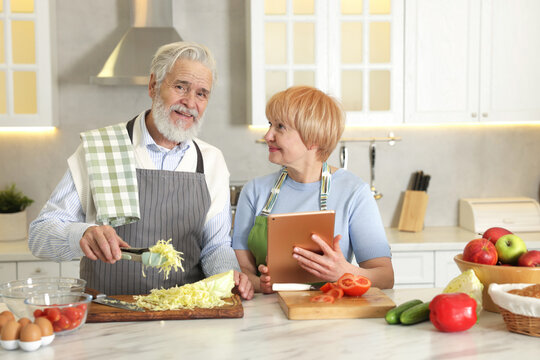 Senior couple using tablet while cooking together in kitchen - Powered by Adobe