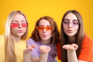 Beautiful women with different hair colors blowing kisses on orange background