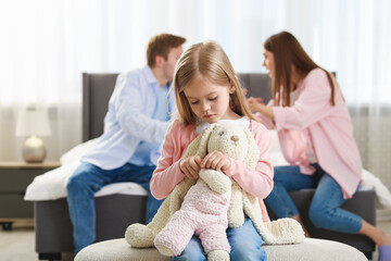 Upset little girl with bunny and her parents fighting at home, selective focus