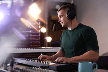 Man in headphones working with MIDI keyboard at table in home studio