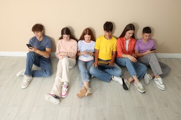 Group of teenagers with laptop and smartphones near beige wall indoors
