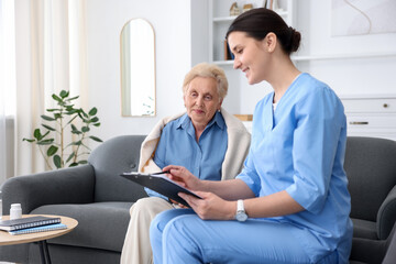 Nurse with clipboard examining senior woman indoors. Home health care service