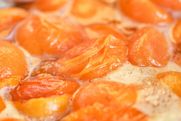 Cooking apricot jam with foam. Orange color apricot berries bubbling in a pot during the simmering process for a fresh homemade jam. Shallow depth of field