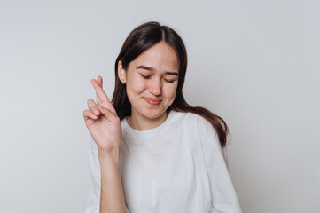 Smiling young woman crossing fingers for good luck in a light studio setting