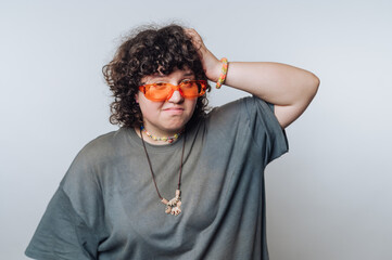 person with curly hair and fun orange sunglasses displays a quirky expression while touching their...