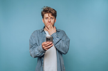 Young man expresses surprise while looking at his smartphone against a blue background