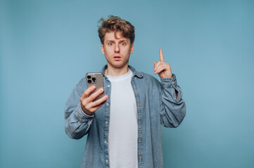 Man with phone showing surprise while standing against a blue background in a casual setting