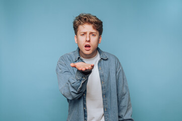 Young man gesturing with palm up while expressing surprise in front of a blue background during a...