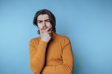 Thoughtful young man poses with a questioning expression against a blue background in a cozy setting