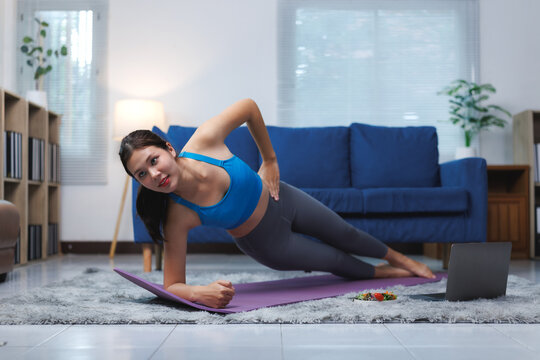 Young asian woman doing side plank exercise at home watching online tutorials on laptop