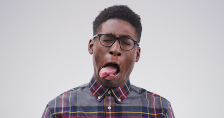 Goofy, black man and funny face with tongue out for joke or comic on a white studio background. Male person, model or humor with glasses, crazy or quirky personality for comedy on mockup space