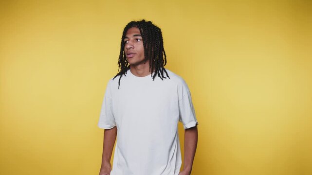 laid-back young man with dreadlocks displays a cool attitude and slight smirk on yellow background