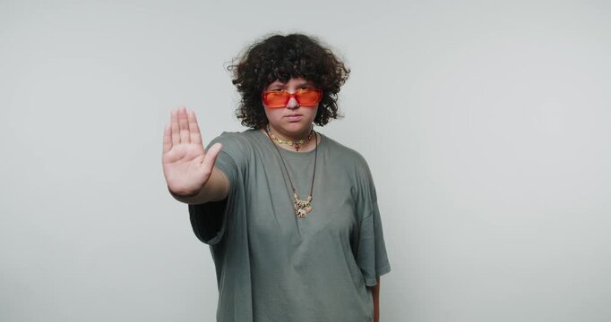 young curly woman in red glasses extends their hand in a halt gesture, promoting themes of self-assertion and boundaries on white background
