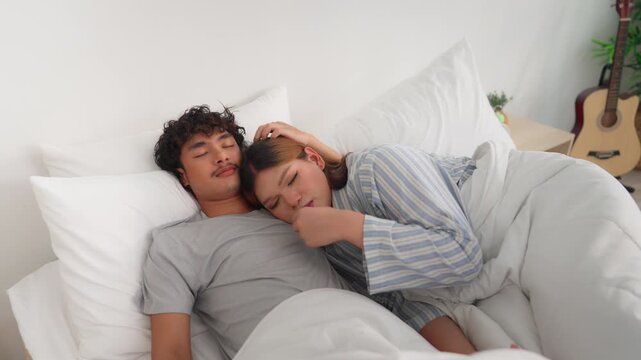 Asian transgender woman and male partner lying down, sleeping on bed. 