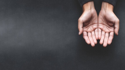 Open hands of a person, palms facing up, resting on a dark textured surface, symbolizing offering, sharing, and connection in a minimalist setting
